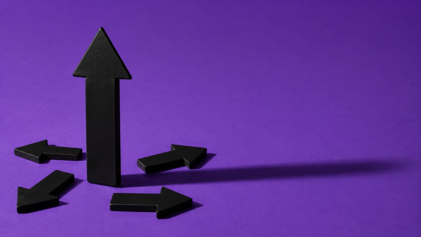 A tall matte-black arrow standing among smaller toppled arrows on a deep violet backdrop