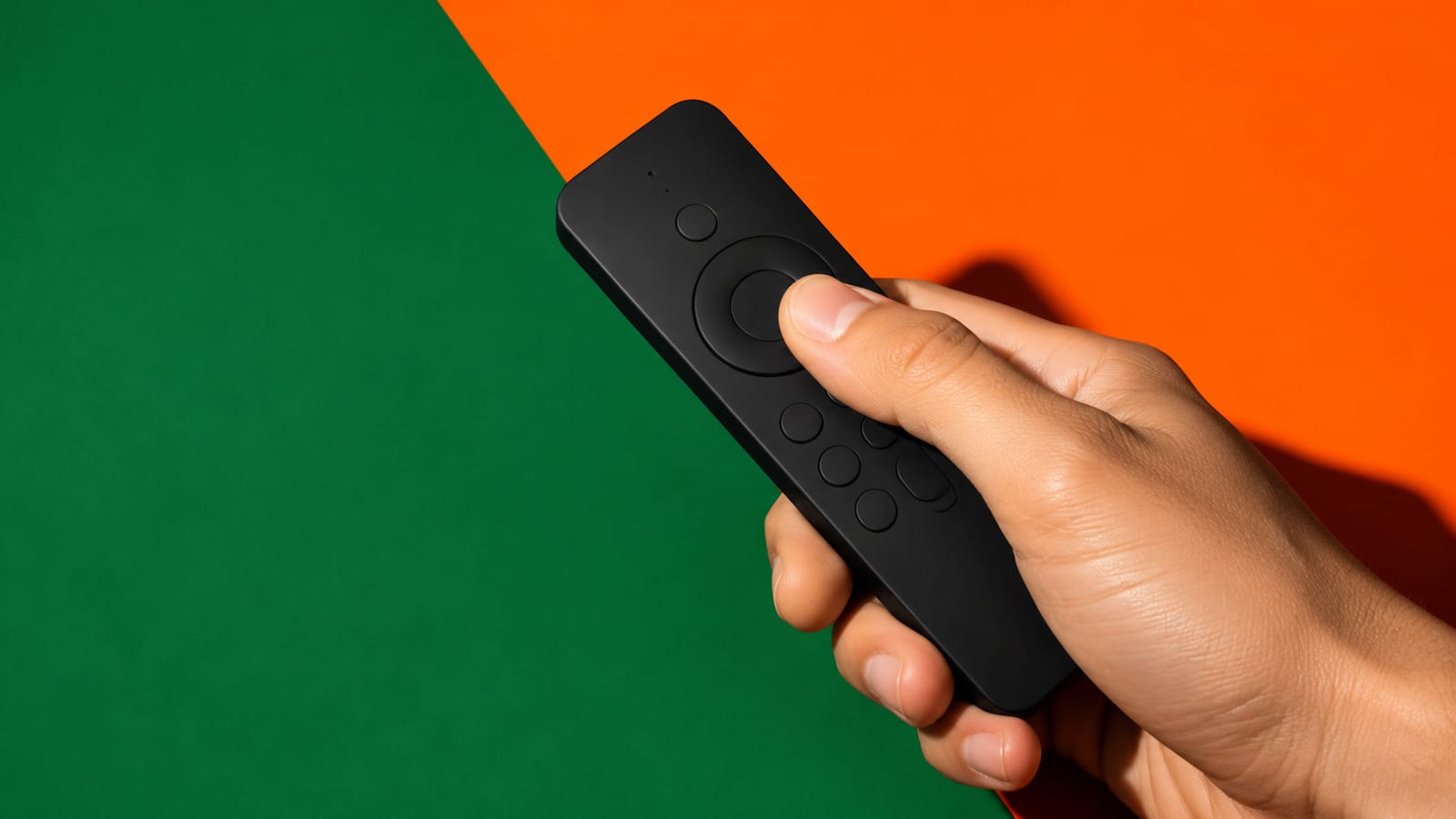 Hand pressing the directional pad of an Android TV remote against a green and orange background