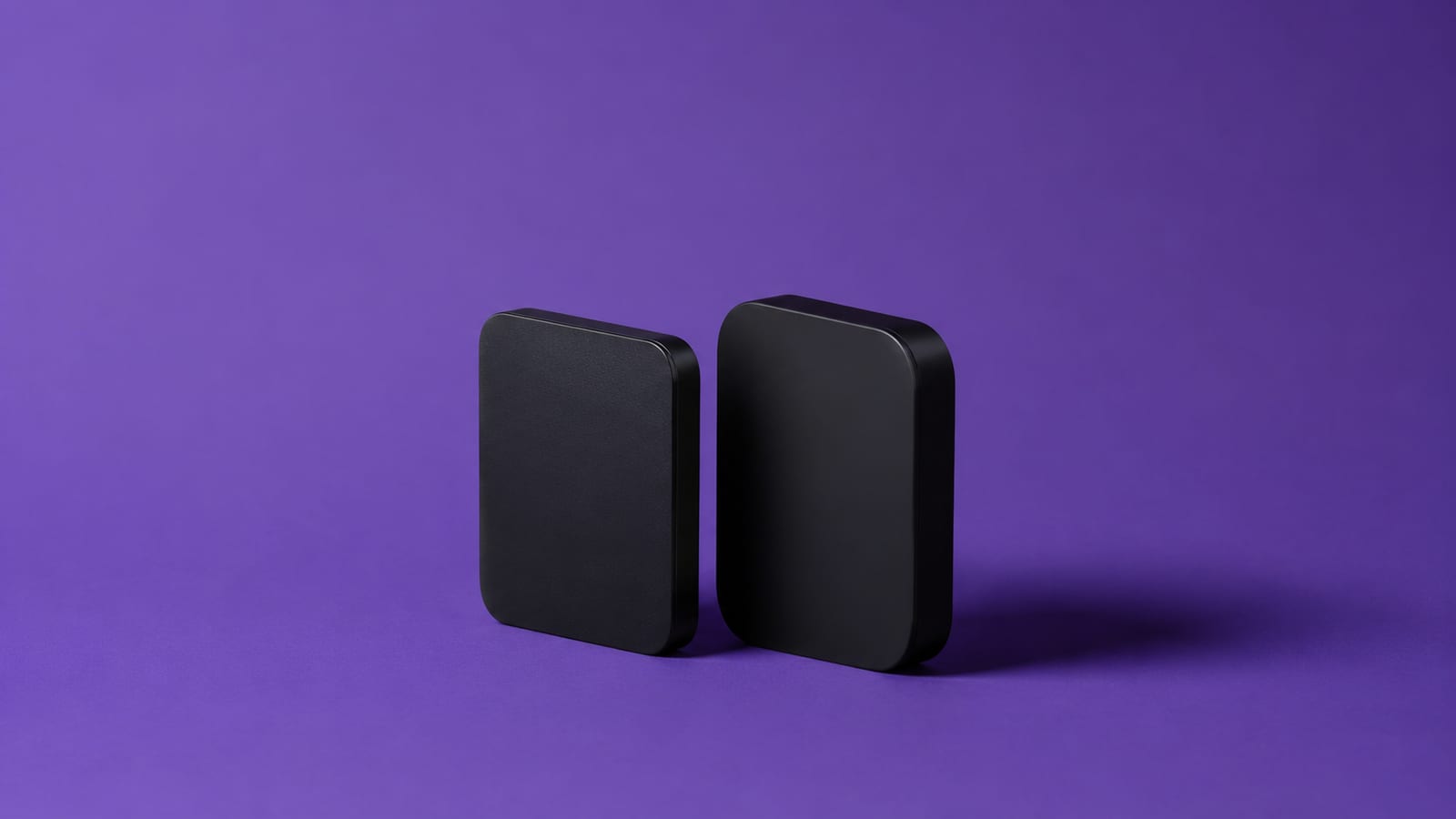 Two matte-black streaming boxes of different sizes standing side by side on a deep violet studio background