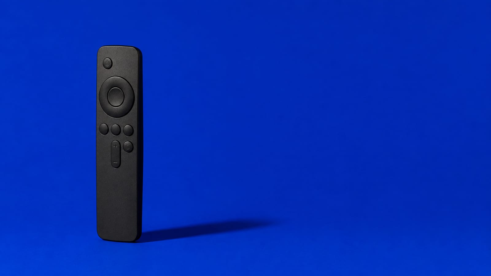 A slim matte-black streaming remote standing upright on a cobalt blue studio background