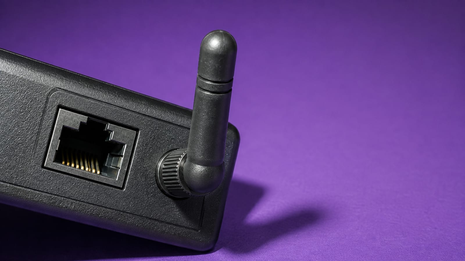 Close-up of an ethernet LAN port and a wireless antenna side by side on a black housing, on a deep violet backdrop