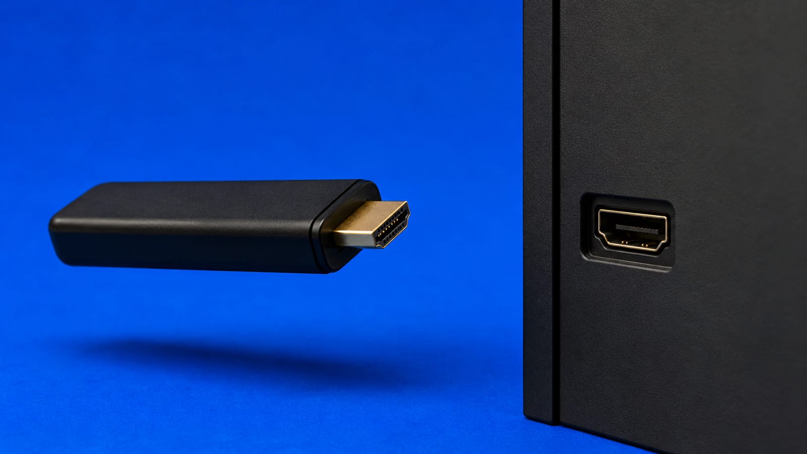 Small matte-black streaming stick floating beside an empty HDMI port on a cobalt blue backdrop