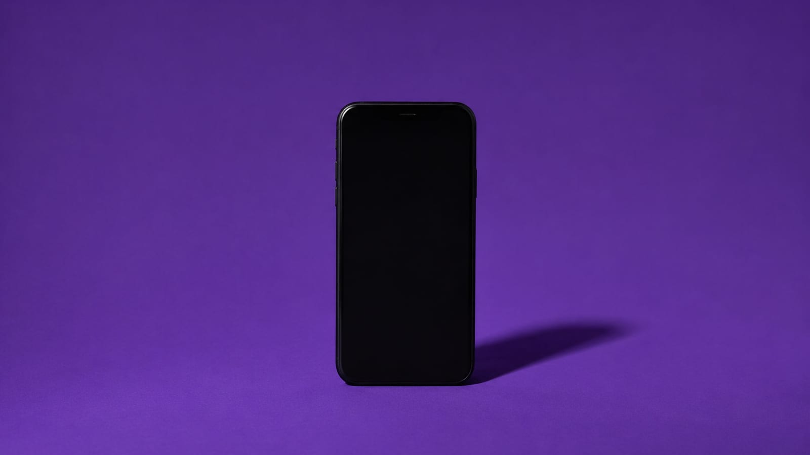 A matte-black smartphone with a blank screen on a deep-violet background