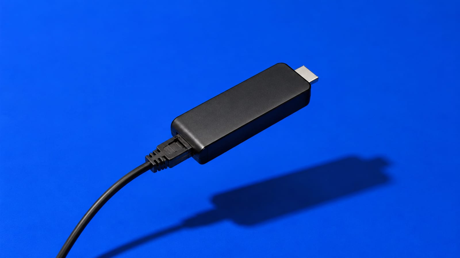 A matte-black HDMI streaming stick with a cable on a cobalt-blue background
